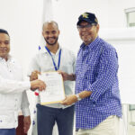 Gonell-Cosme-acompanado-de-Pablo-Portes-agente-de-atencion-al-usiario-entrega-el-certificado-a-Fernando-Villalona.